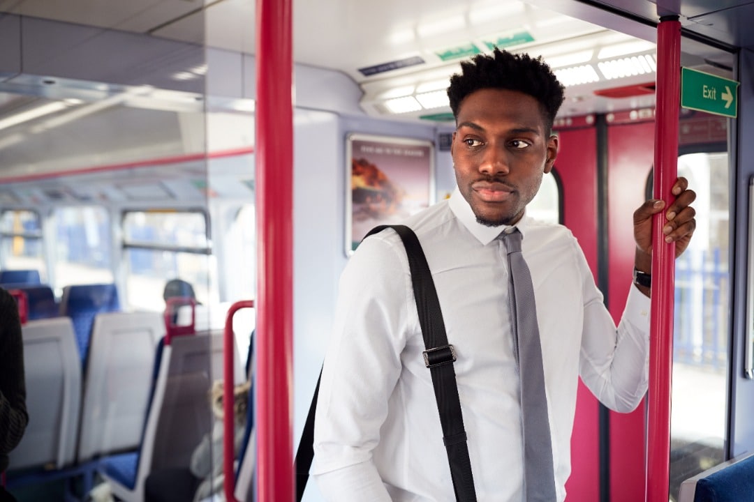 Man in a dress shirt and tie standing on a bus on his way to work.