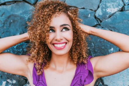 close up of woman in purple tank top putting her hands behind her head and looking to the side