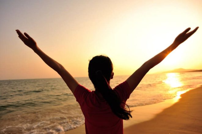 cheering woman open arms at sunset seaside beach